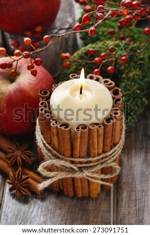 Candle decorated with cinnamon sticks and red apples