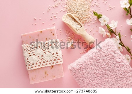 Pink spa set: bar of handmade soap, sea salt and towel. Blooming cherry twigs in the background.