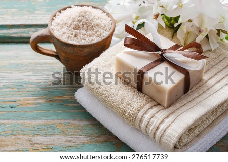 Spa set: bar of handmade natural soap lying on the towels, cup of sea salt and alstroemeria flowers