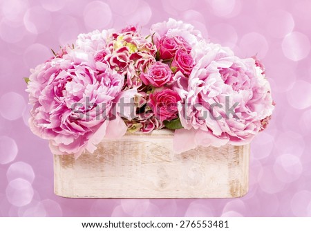 Pink peonies and roses in wooden box. Pink glittering, blurred, abstract background.
