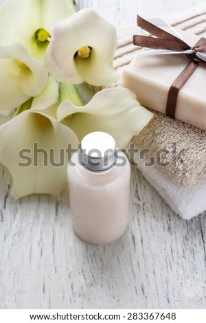Bar of handmade natural soap, liquid soap, towels and bouquet of white calla flowers on rustic wooden table