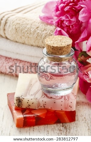 Bottle of essential oil and bars of natural handmade soap, soft towels in the background.