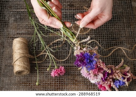 Florist at work. Woman making wreath with wild flowers.