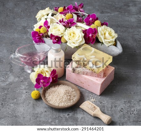 Spa set: sea salt, bars of handmade soap and liquid soap. Bouquet of flowers in the background.