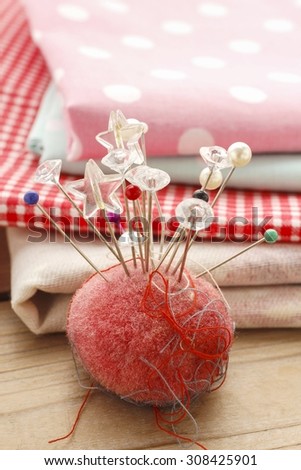 Pin cushion with sewing pins, colorful fabrics in the background