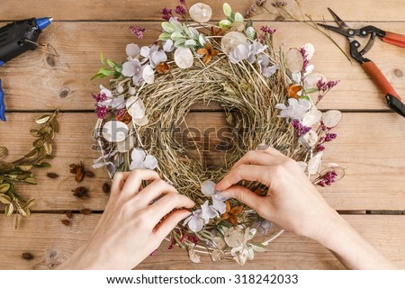 Florist at work: woman making door wreath with autumn plants and flowers