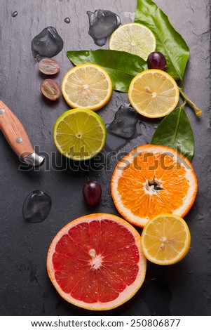 Set of sliced citrus fruits lemon, lime, orange, grapefruit with  ice and vintage knife over stone black background. Top view.