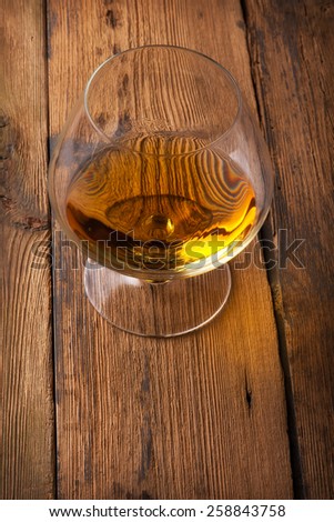 Glowing cognac or brandy in an elegant snifter glass on an old dark wooden bar counter with copyspace
