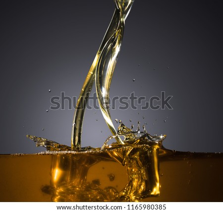 Close-up of oil and liquid pouring  with splashing on dark background. Isolated studio shooting