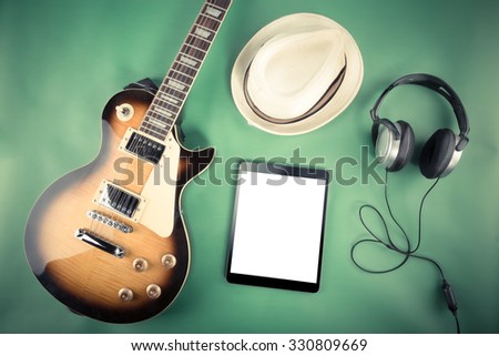 Electric guitar with tablet, hat and headphones on green background