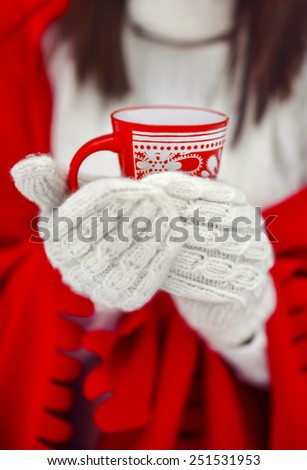 the girl in mittens holds a red cup in hand