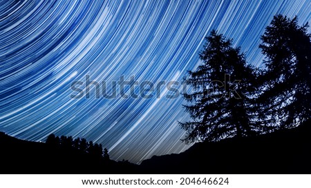 Star trail effect over mountain and trees in night sky