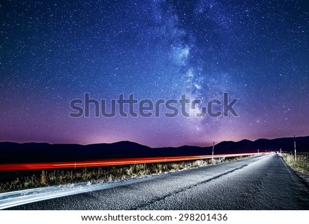 Night sky with milky way and stars. Night road illuminated by car. Light trails