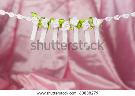 A row of clothes pegs - pins with little white textile flowers and green leaves, hanging on a white string - pink background.