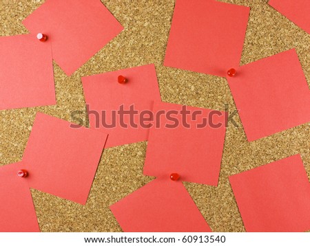 A bulletin cork board background with messy square pieces of blank red post-it paper notes.