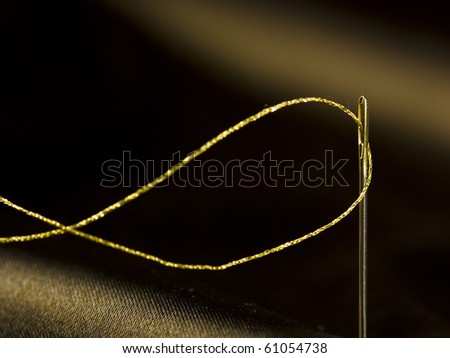 Detail of a needle with golden cotton thread on satin background.