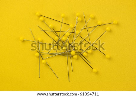 Detail of yellow sewing pins on yellow textile background.