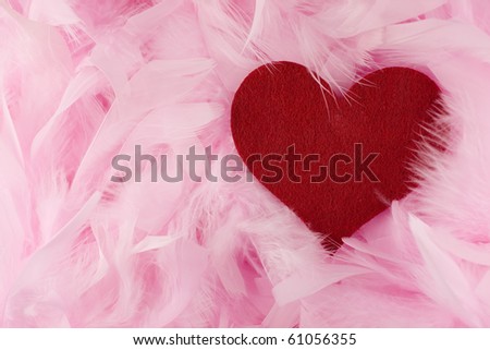 Valentin love theme - red fabric heart lying in pink feathers background.