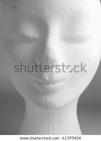 A head of an old female mannequin fashion head painted white, worn and used with cracks and scratches.