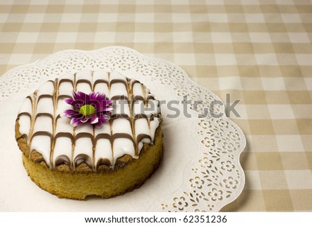 Baked fancy cake with a purple flower on a table with soft beige square cloth.
