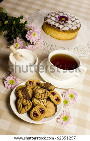 An afternoon tea theme with biscuits, cake, sugar and flowers in beige and pink - cozy still life.