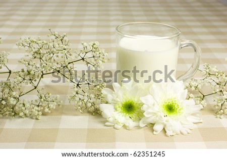 A glass cup with milk on table country like cloth  with white flowers.