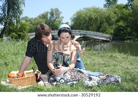 Couple sitting together by a lake with a picnic basket.