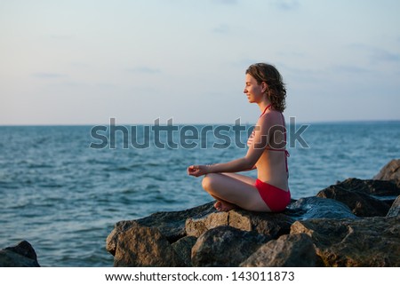 Woman that meditates at the sea during sunset