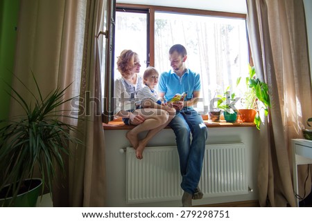 Happy family sitting on a window sill and read a book.