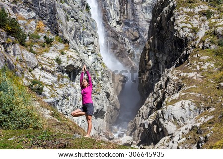 Caucasian woman is doing yoga exercises in mountains in front of big waterfall