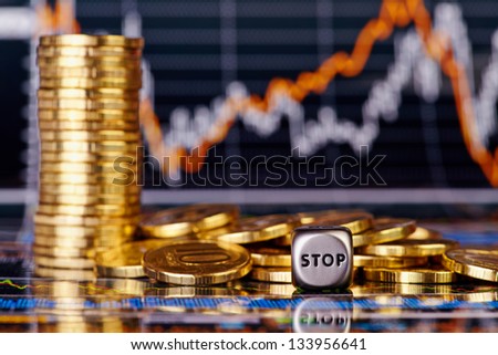 Dices cube with the word STOP golden coins. Financial stock charts as background. Selective focus