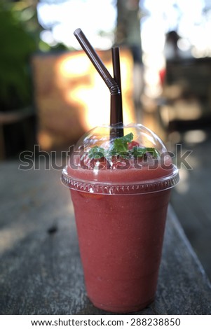 strawberry smoothie in a glass with frozen strawberry and mint leaf on top