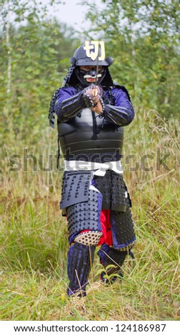 Man in Japanese medieval samurai armor (tosei-gusoku) standing in combat position with Japanese sword katana