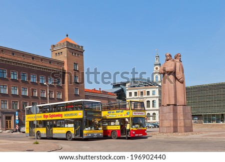Riga, Latvia - May 25, 2014: Two yellow double-decker city sightseeing buses waiting for tourists on the Latvian Riflemen square in Riga, Latvia