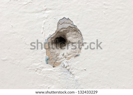 Deep circular hole in the plaster wall covered with peeling paint