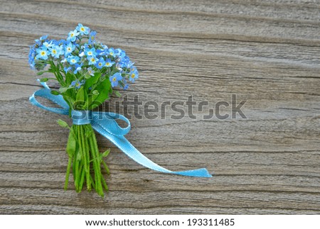 Small bouquet of blue forget-me-not, tied a blue ribbon, on the background of old wooden plank