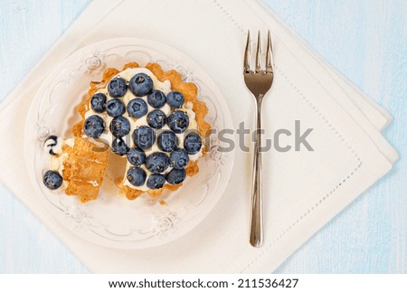 Cheesecake with fresh blueberries on a decorative plate with dessert fork and a beige linen napkin