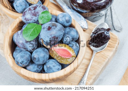 Blue ripe plums in wooden bowl and jam in a glass jar