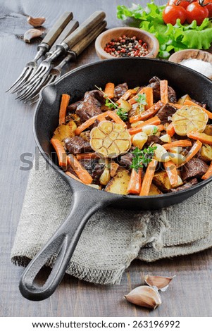 Roast meat with vegetables in a cast iron skillet on a wooden table