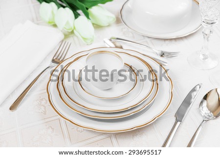Beautifully decorated table with white plates, crystal glasses, linen napkin, cutlery and tulip flowers on luxurious tablecloths