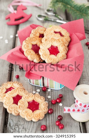 Sweet Christmas cookies with jam, fir branches and cones, cranberries, spool with decorative ribbon and red toy rocking horse on the old wooden table