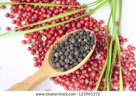 A spoon of black pepper on rose pepper spilled over the table
