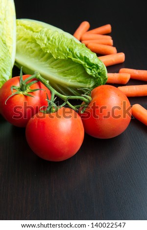 A bunch of tomatoes, baby carrots and romaine hearts on a black wooden table vegetable mix