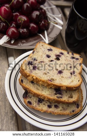 Blueberry bread with red cherries and tea on a wooden table