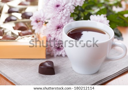 White tea cub with a box of chocolate sweets and flowers