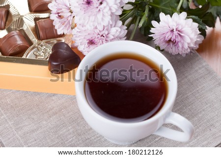 White tea cub with a box of chocolate sweets and flowers