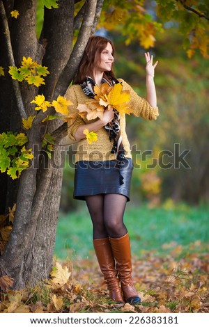 beautiful  smiling woman beige sweater and black leather skirt posing in autumn nature background near the tree