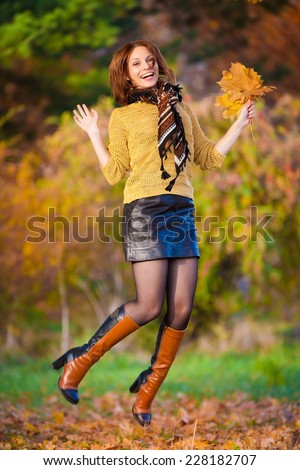 beautiful  smiling woman beige sweater and black leather skirt jump in autumn nature background
