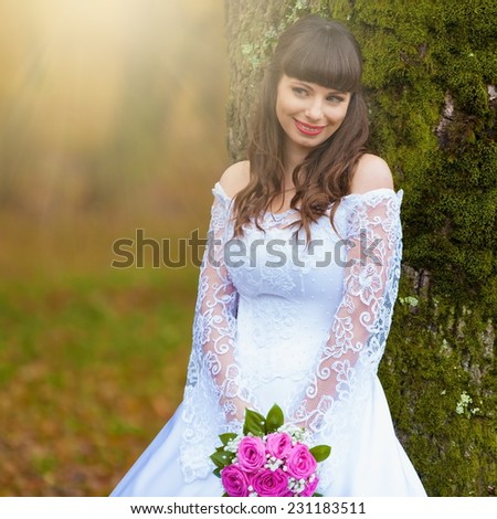 beautiful and happy smiling  brunette bride in white lacy satin dress european style with  bouquet of pink roses autumn background