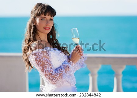 beautiful and happy smiling  brunette bride in white lacy satin dress european style with  glass of champagne sea background